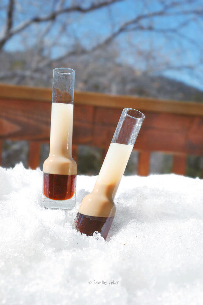 Two tall slender shot glasses in the snow with B52 cocktail in it