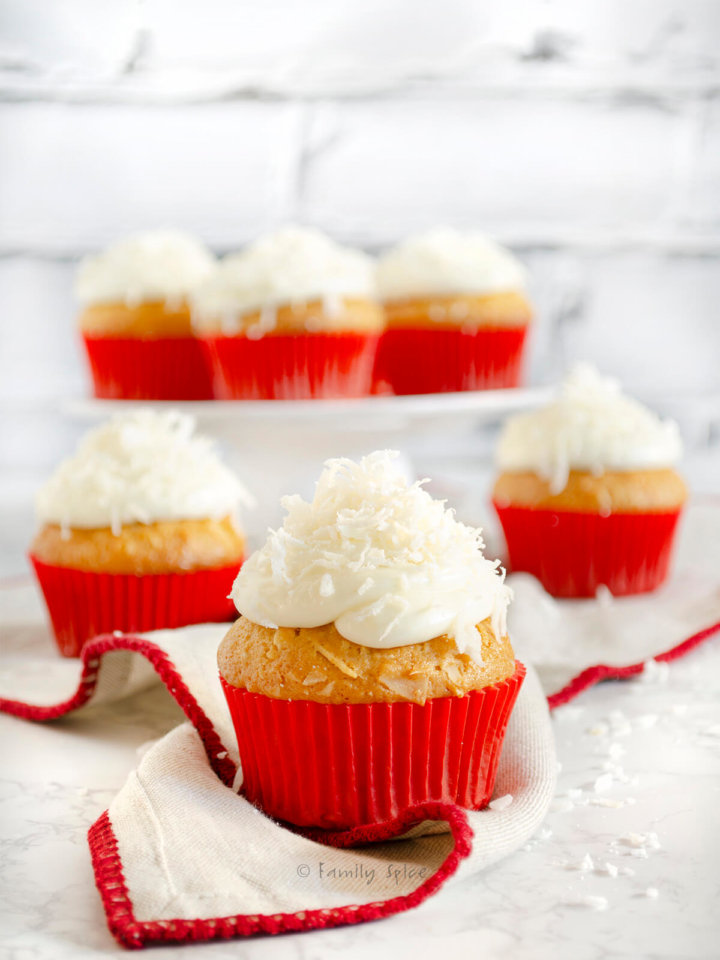 An assortment of coconut cupcakes topped with coconut in red cupcake liners