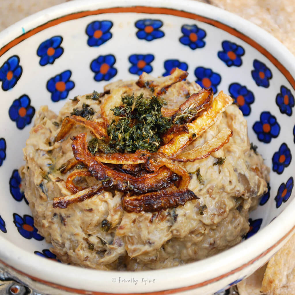 A decorative bowl with kashkeh bademjan and garnished with caramelized onions, dried mint and olive oil