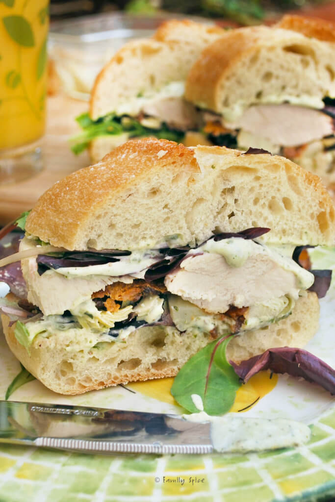 Closeup of a chicken sandwiches with bacon and caesar dressing with more sandwiches behind it