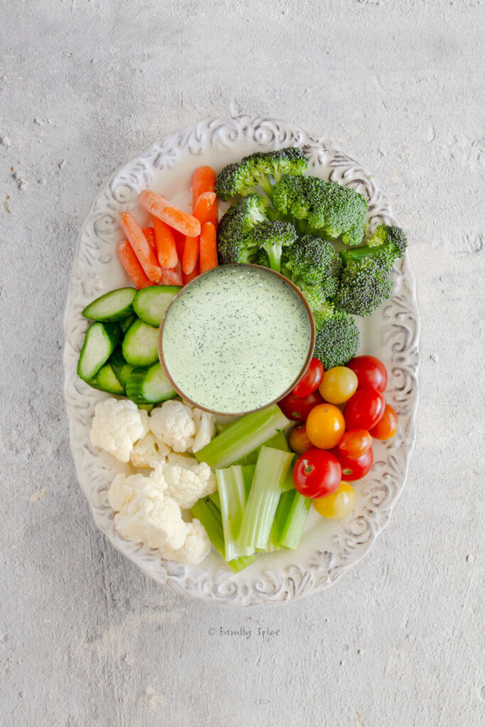 Homemade caesar dressing with assorted raw vegetables on a white oval plate