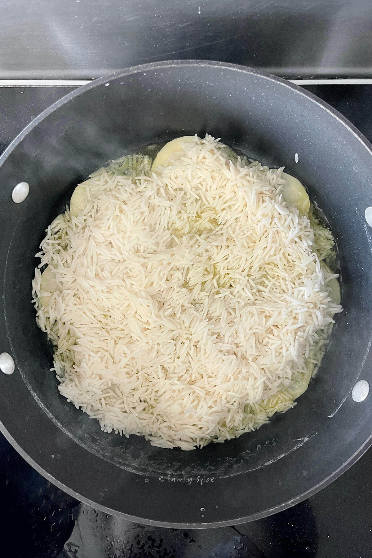 Top view of a non-stick pot with potato slices on the bottom and a layer of parboiled basmati rice