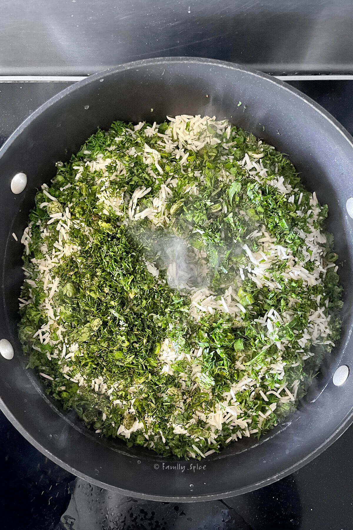 Top view of a non-stick pot with layers of rice and chopped herbs and a hole in the center with steam coming out