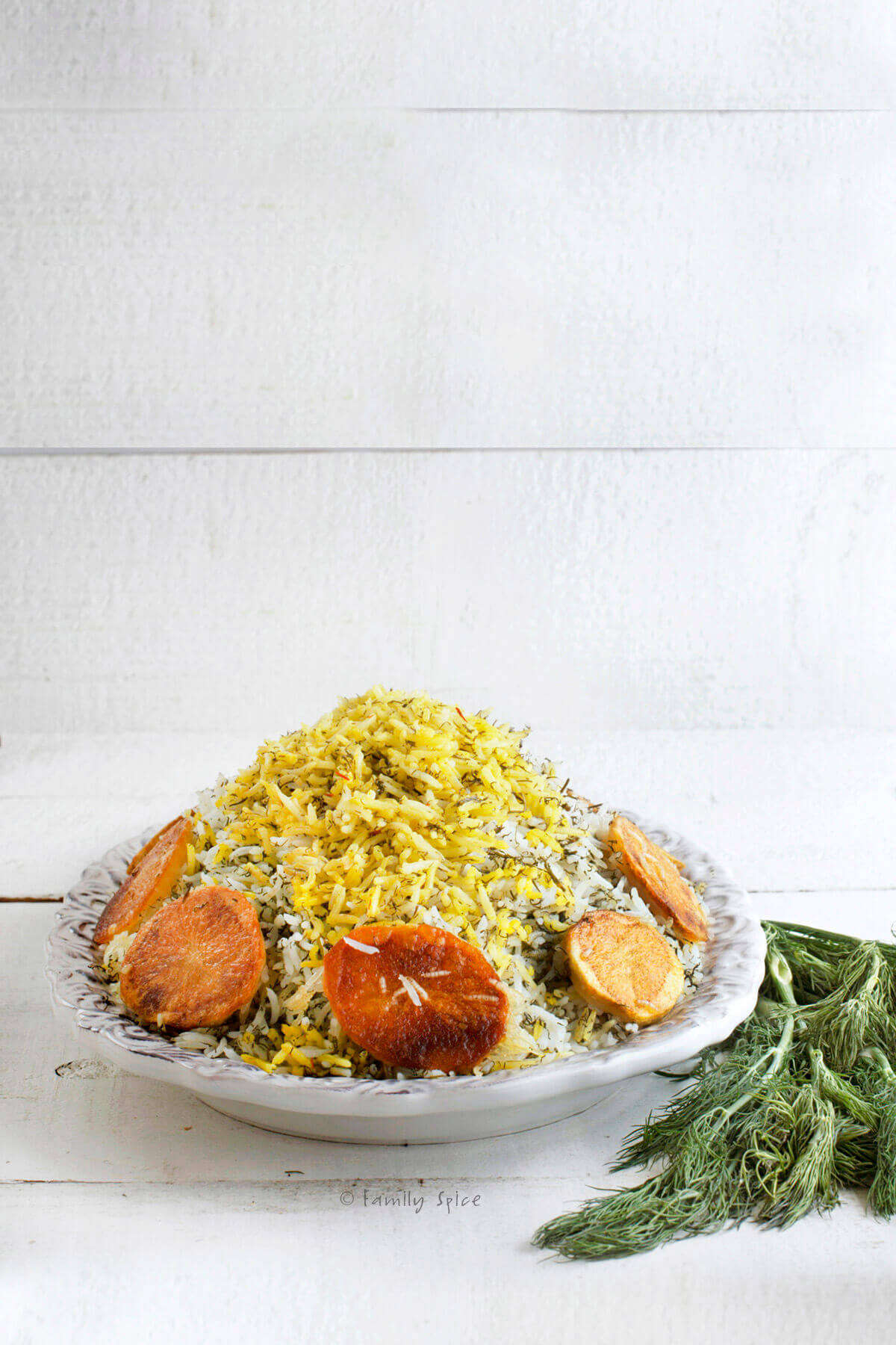 Side view of an oval platter with sabzi pollo (Persian herb rice) topped with saffron rice and surrounded with crispy potato rounds 