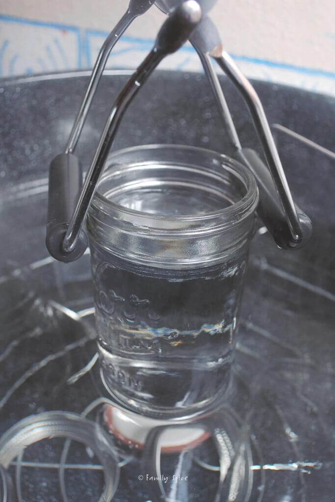 Pulling out a glass mason jar out of a large pot with hot water