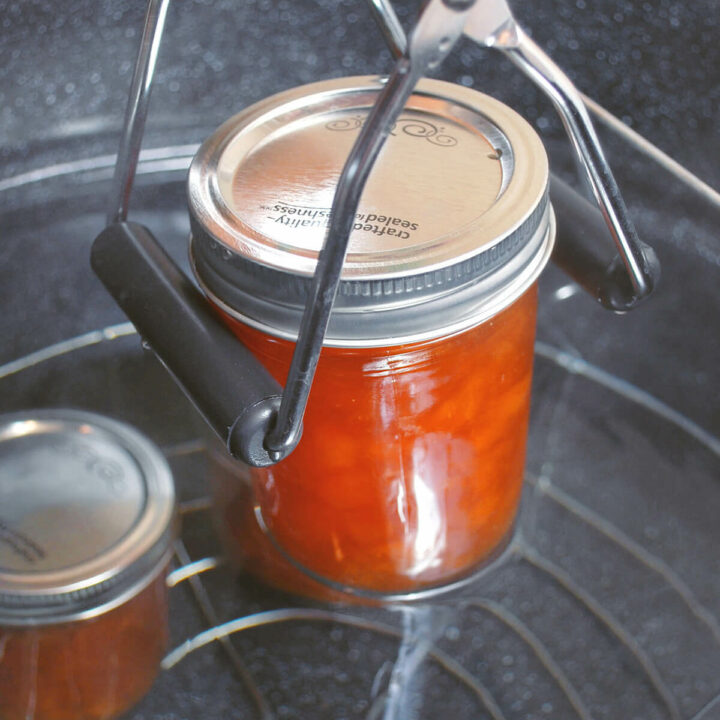 Placing a mason jar with peach jam in a large pot of hot water to hot water can
