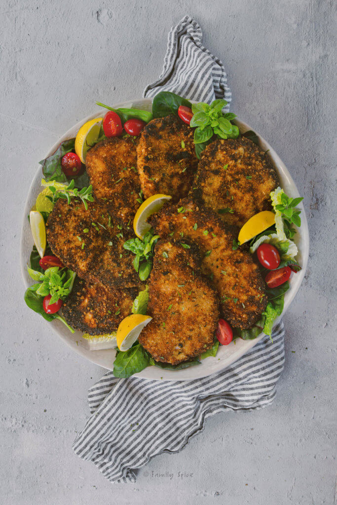 A platter of pork Milanese cutlets with greens, lemon wedges and tomatoes