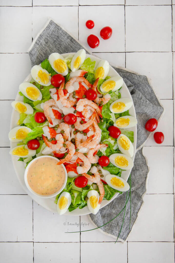 Top view of an oval platter with shrimp and crab louie salad arranged neatly and a bowl of louie dressing next to it