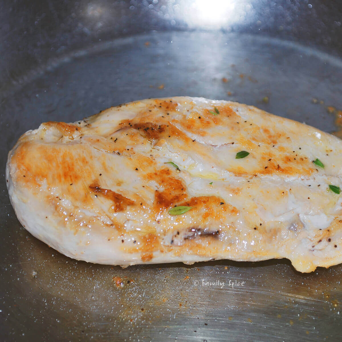 A chicken breast browned in a stainless pan
