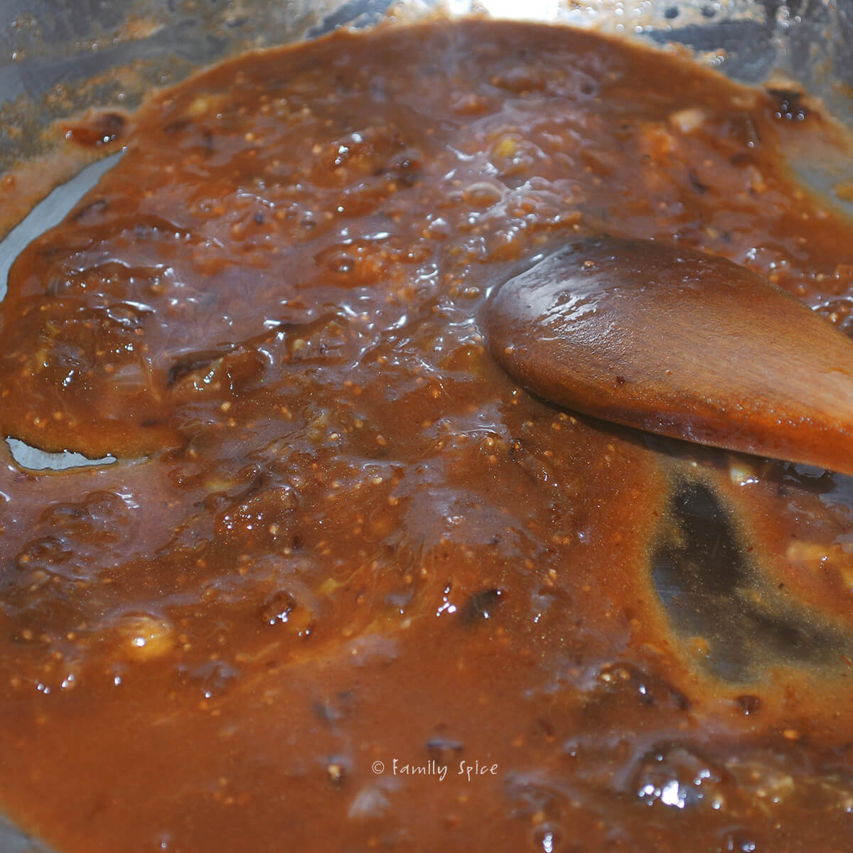 Stirring homemade fig sauce with a wooden spoon in a stainless pan