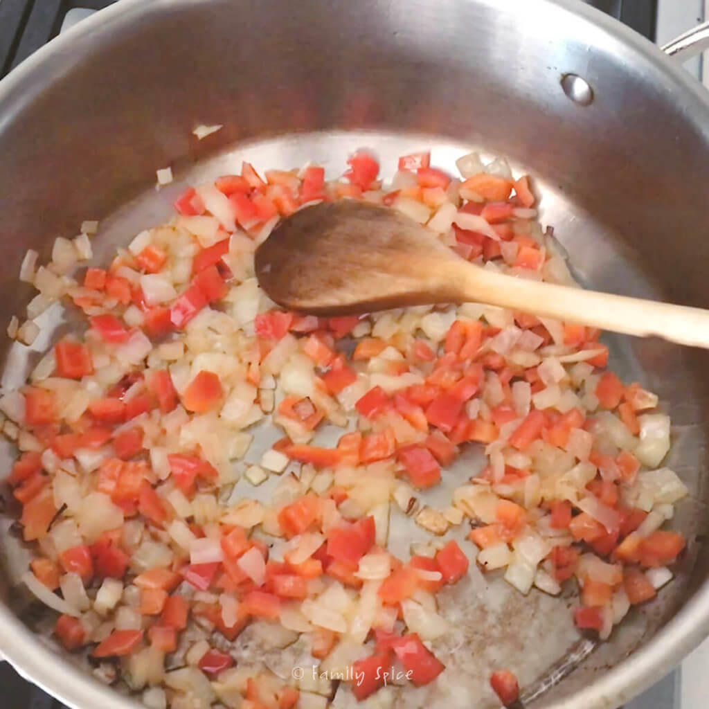 Sautéeing chopped onions and red bell peppers in a stainless pot