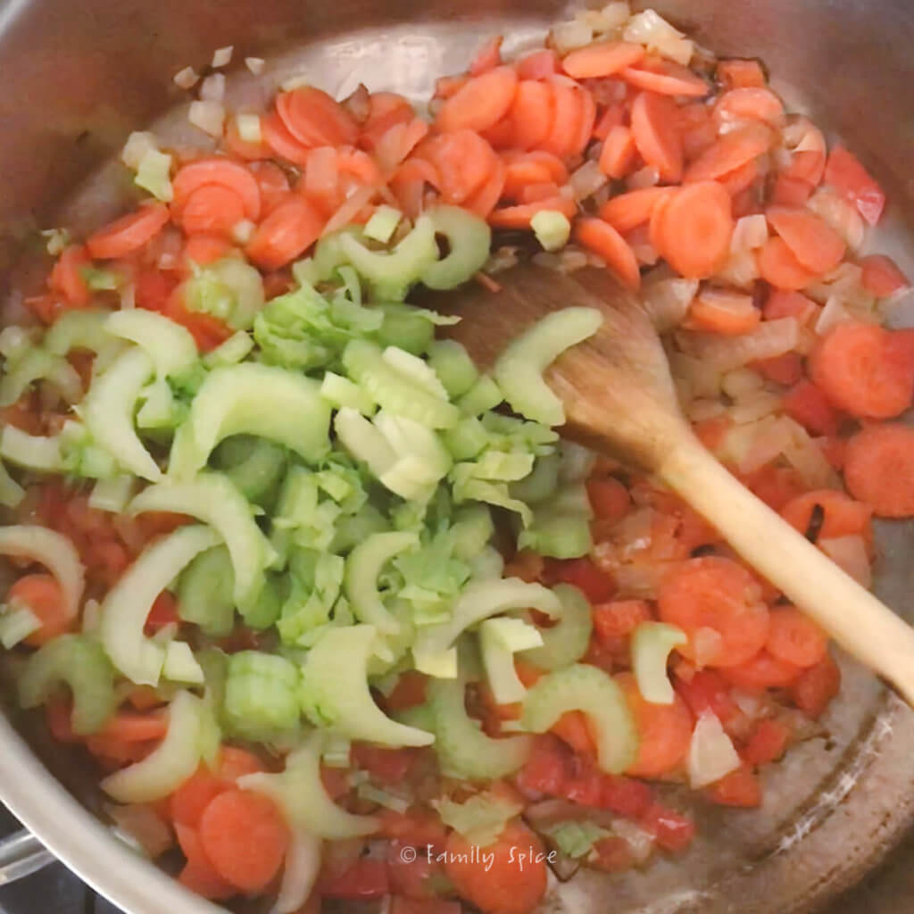 Sautéeing chopped onions, red bell peppers, carrots and celery in a stainless pot