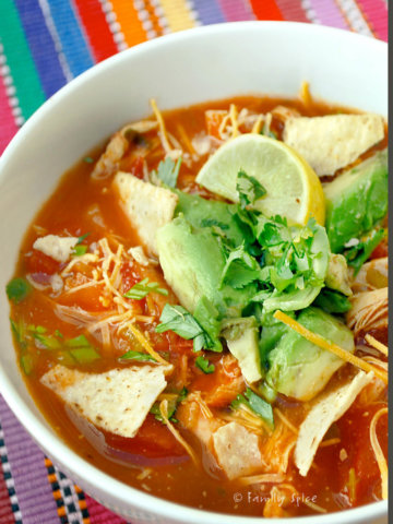 A bowl of chicken tortilla soup garnished with tortilla chips, cilantro and avocado