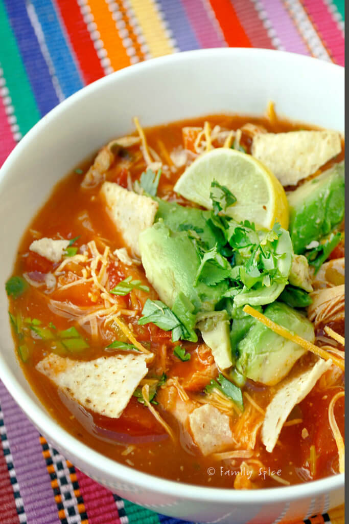 A bowl of chicken tortilla soup garnished with tortilla chips, cilantro and avocado