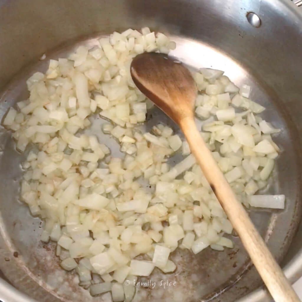 Browning chopped onions in a stainless pot with a wooden spoon