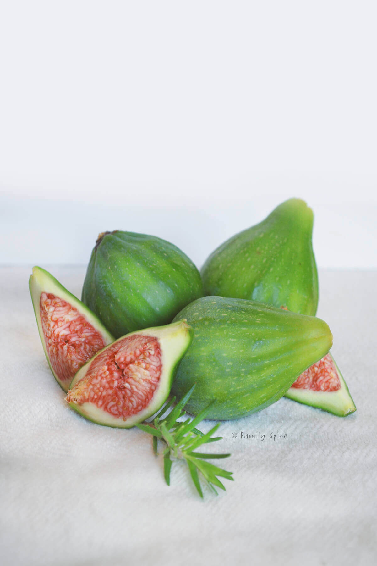 Several fresh green figs with one quartered on a white background