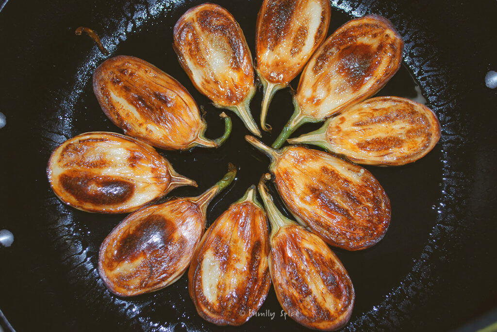 Browning halved baby eggplant in a pan