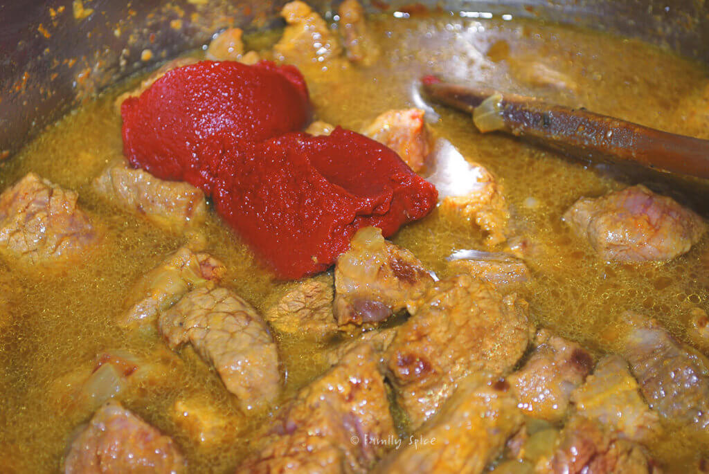 Browned stew meat with tomato paste added to it