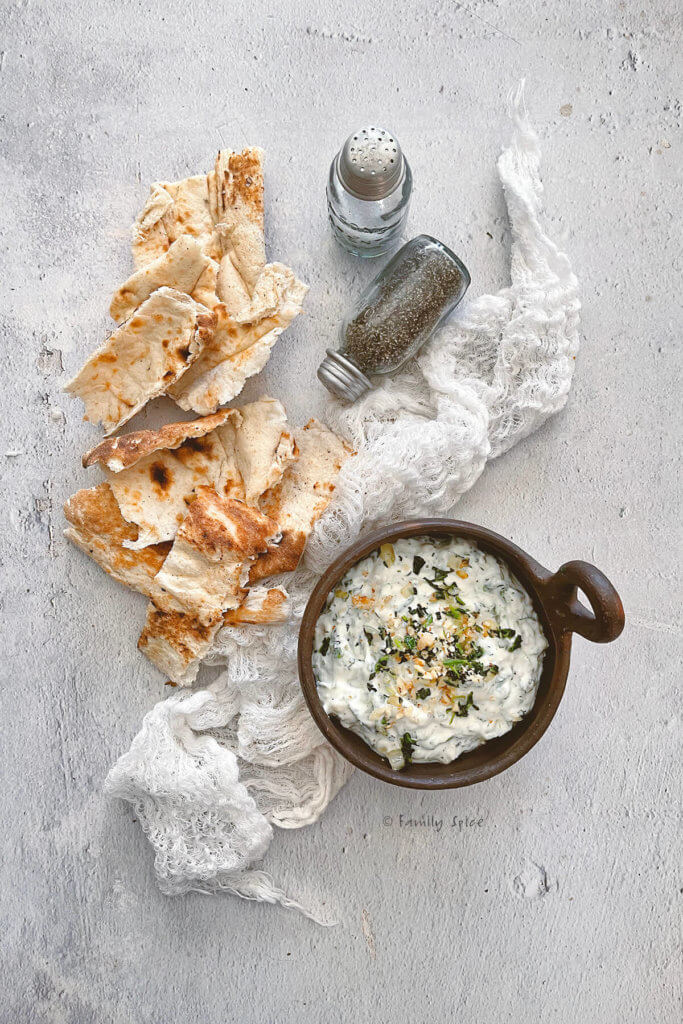 A small brown bowl with borani esfenaj (yogurt spinach dip) in it and torn pieces of flat bread next to it