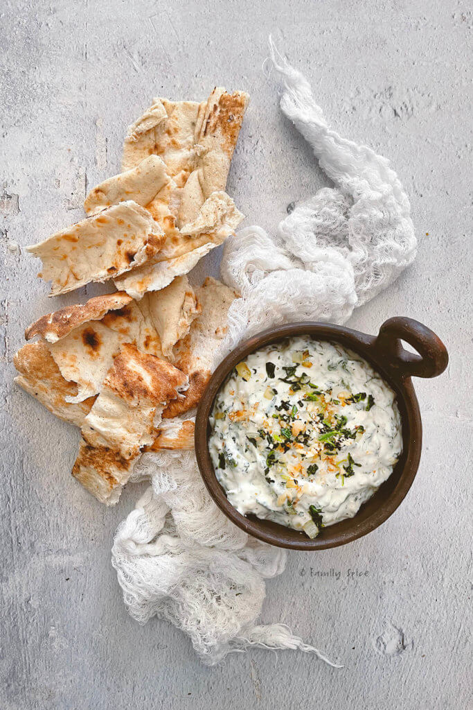 Close up of small brown bowl with borani esfenaj (yogurt spinach dip) in it and torn pieces of flat bread next to it