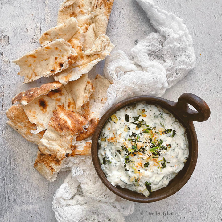 Close up of small brown bowl with borani esfenaj (yogurt spinach dip) in it and torn pieces of flat bread next to it