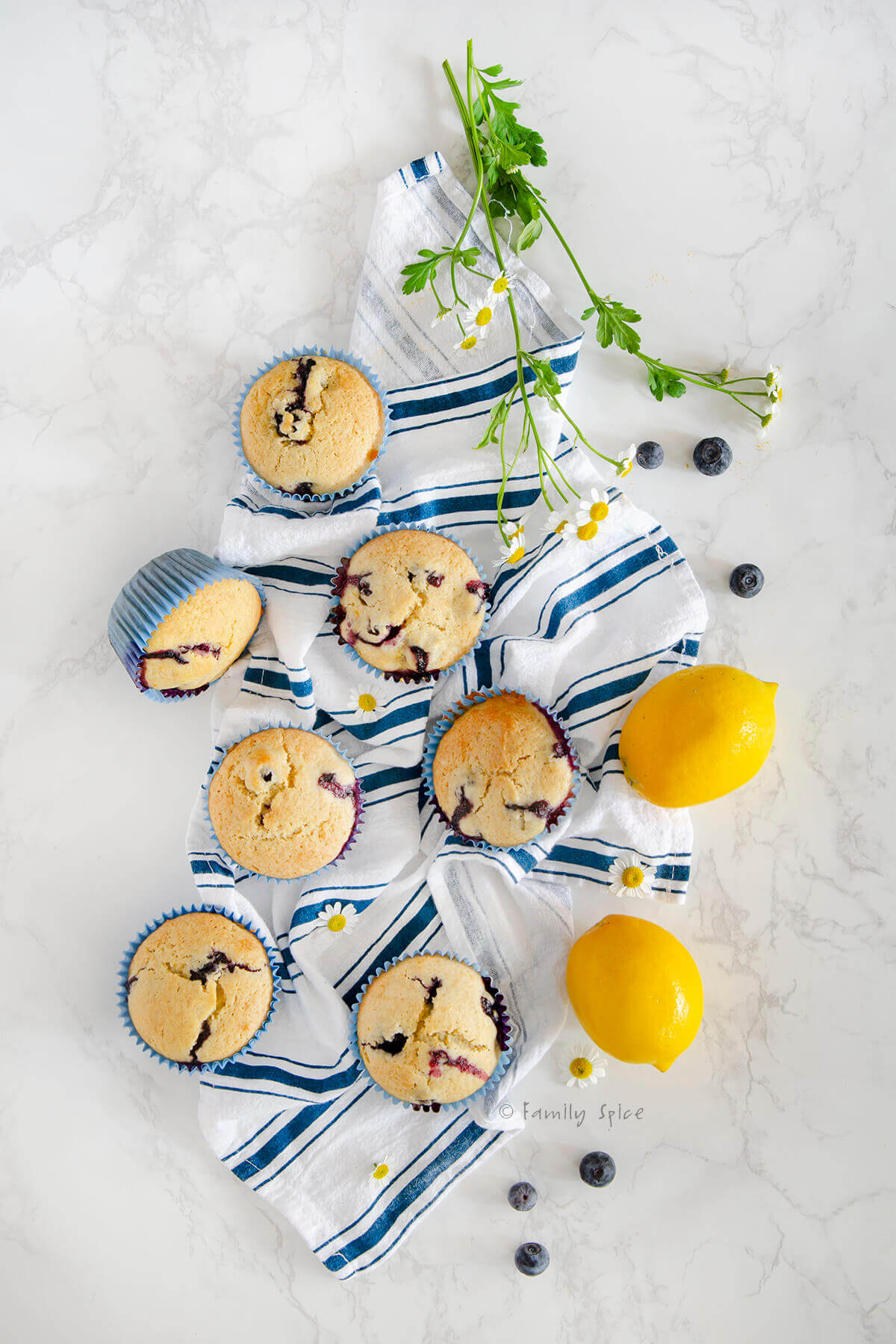 Overhead view of several lemon blueberry muffins on a blue striped dish towel with two lemons