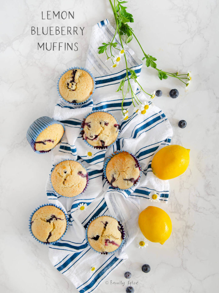 Overhead shot of several lemon blueberry muffins on a white marble background with a blue stripped dish towel by FamilySpice.com