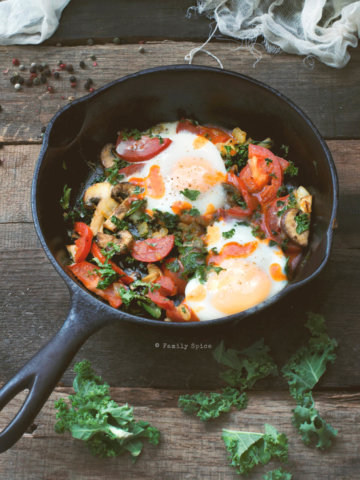 A cast iron skillet with baked eggs, tomatoes, mushrooms and kale