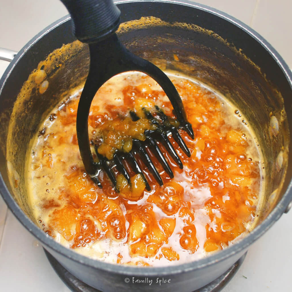 Mashing cooked peach jam with a potato masher