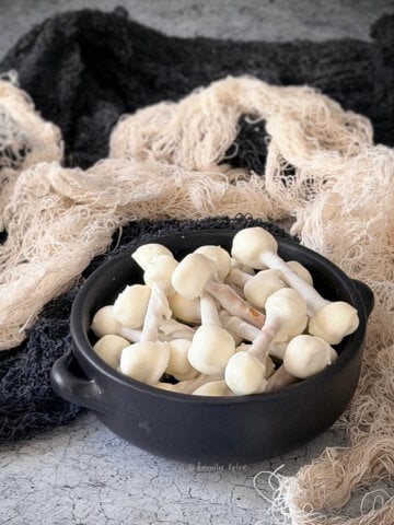 Side view of a black bowl with edible skeleton bones with a spooky background.
