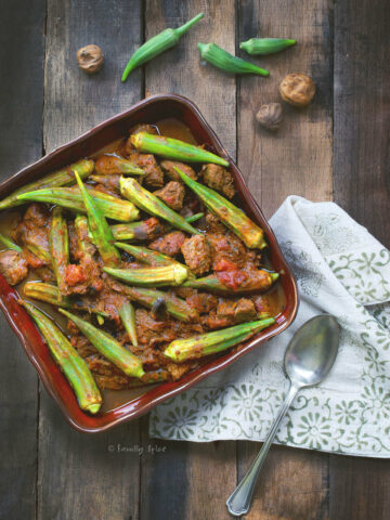 Top view of Persian okra stew with beef in a red square dish on a rustic wood background