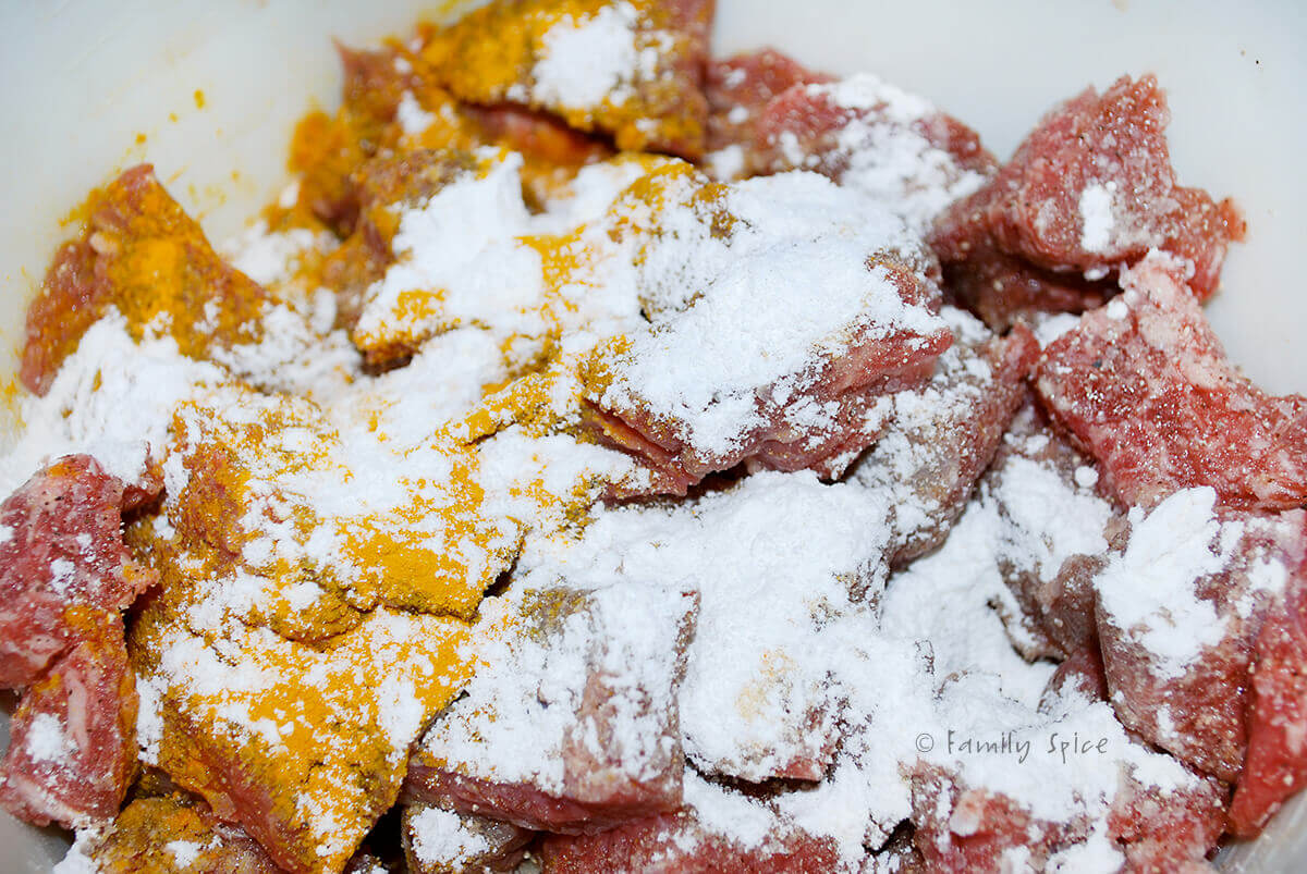 Closeup of chunks of beef stew meat dusted with salt, pepper, turmeric and flour