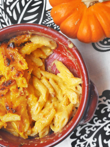 A bowl of pumpkin mac and cheese with a small pumpkin next to it