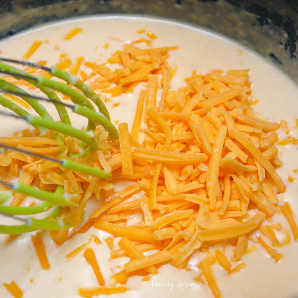 Stirring in shredded cheddar into cheese mixture for mac and cheese
