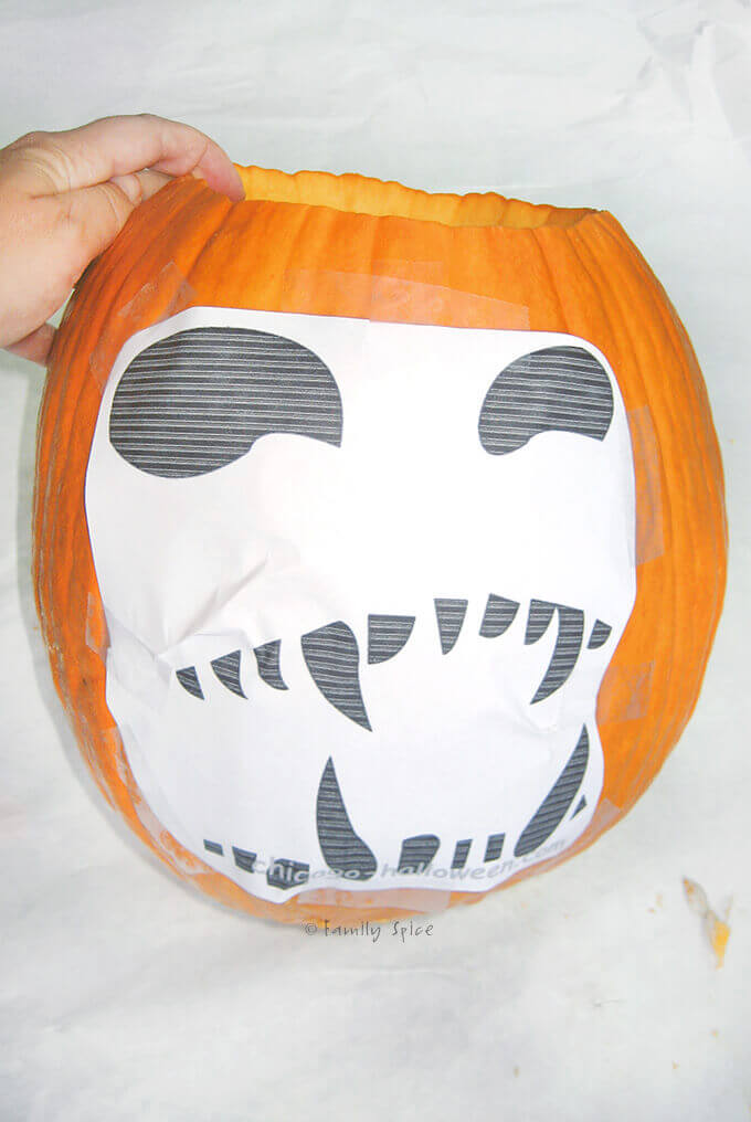 A stencil taped to a pumpkin ready to be carved by FamilySpice.com
