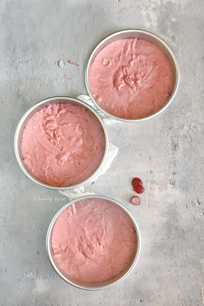 Pink strawberry cake batter in 3 baking pans ready to be baked