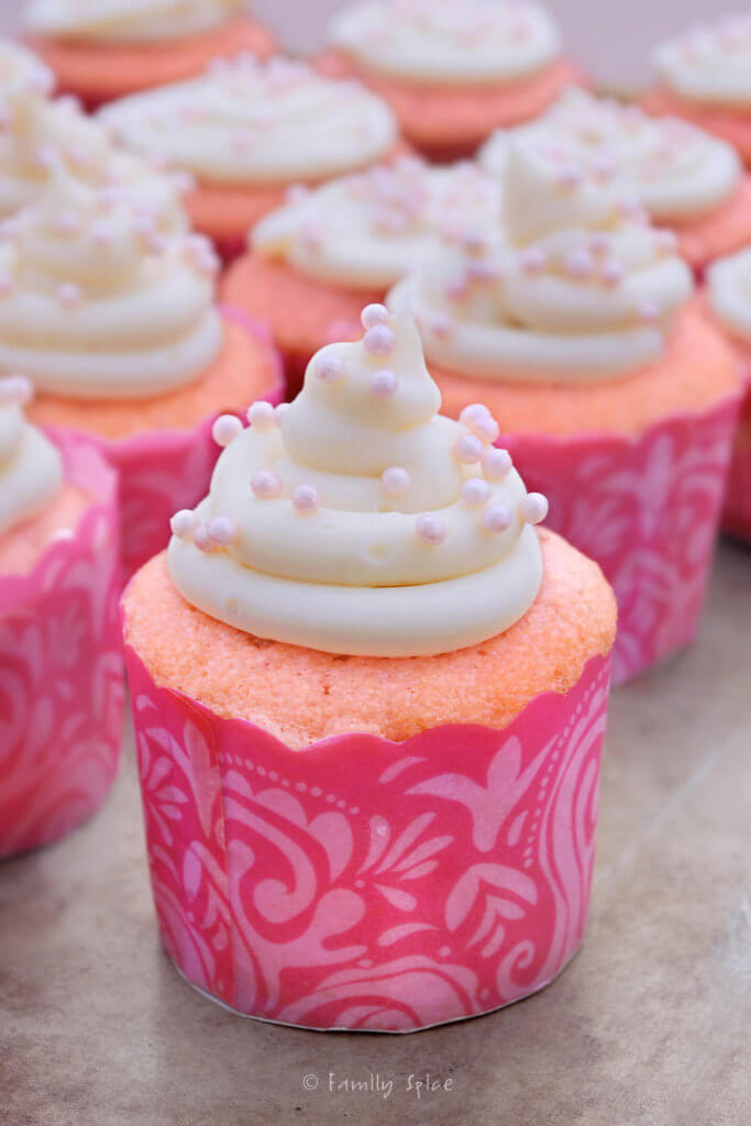 Strawberry cupcakes in pink paper lines topped with cream cheese frosting and candy pink pearls
