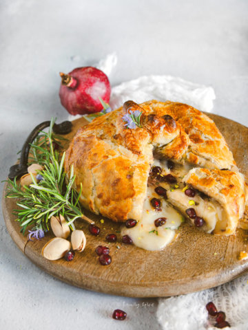 Baked brie wrapped in puff pastry and stuffed with pomegranate and nuts cut open on a round wooden tray