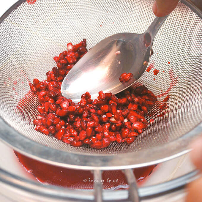 Juicing pomegranate seeds with a strainer by FamilySpice.com