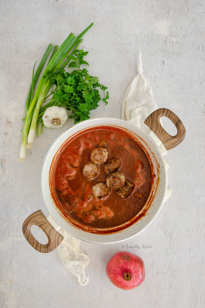 A white pot with tomato pomegranate sauce and meatballs in it