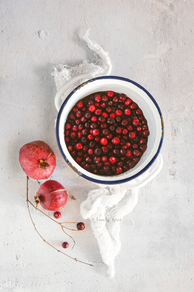 Cranberries in a white enamel pot with fresh pomegranate next to it