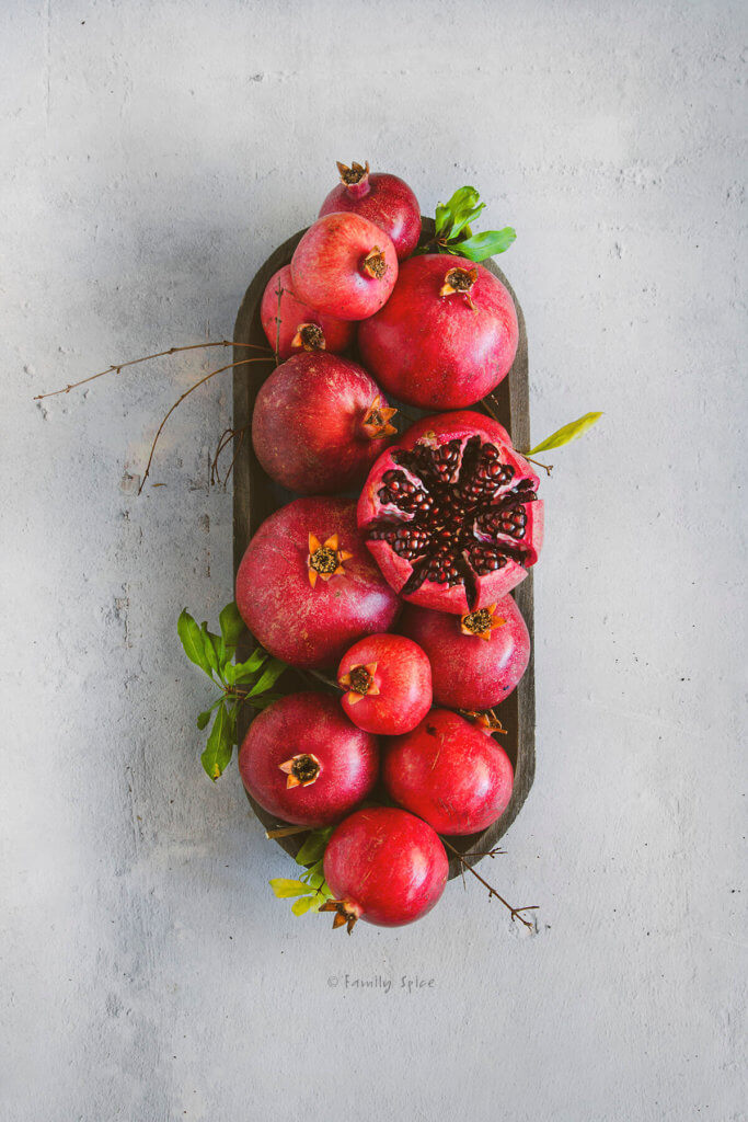 Overhead view of a wooden tray with pomegranates and one cut open