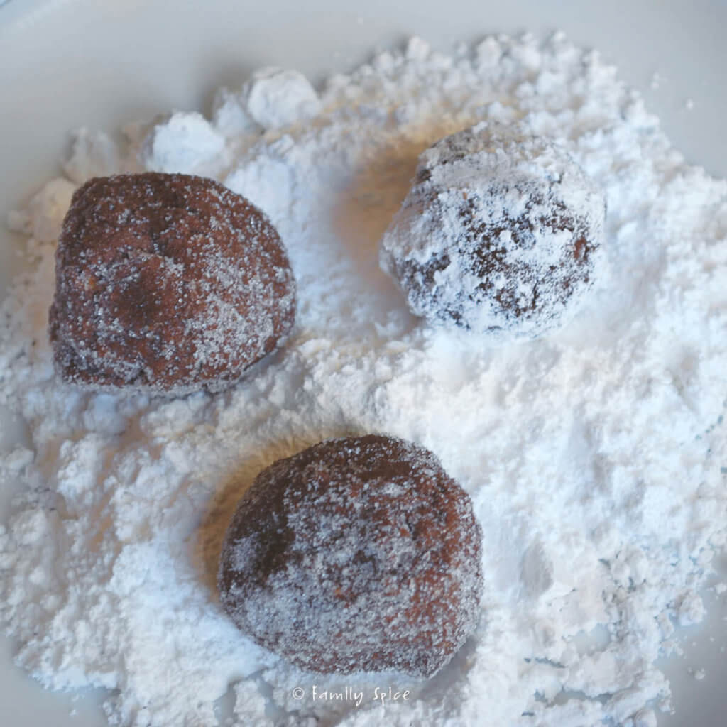 Rolling balls of chocolate cookie dough in powdered sugar
