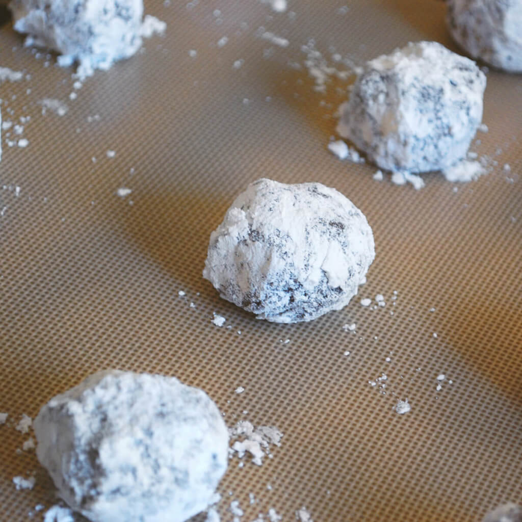 Chocolate snowball cookies covered in powdered sugar on a baking sheet