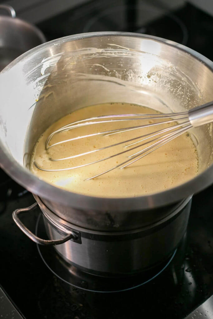 A double boiler with a stainless bowl whisking up hollandaise sauce