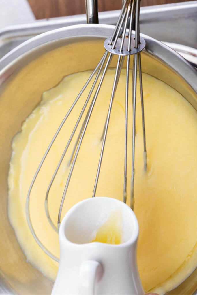 Whisking hollandaise sauce in a metal pot and pouring in lemon juice