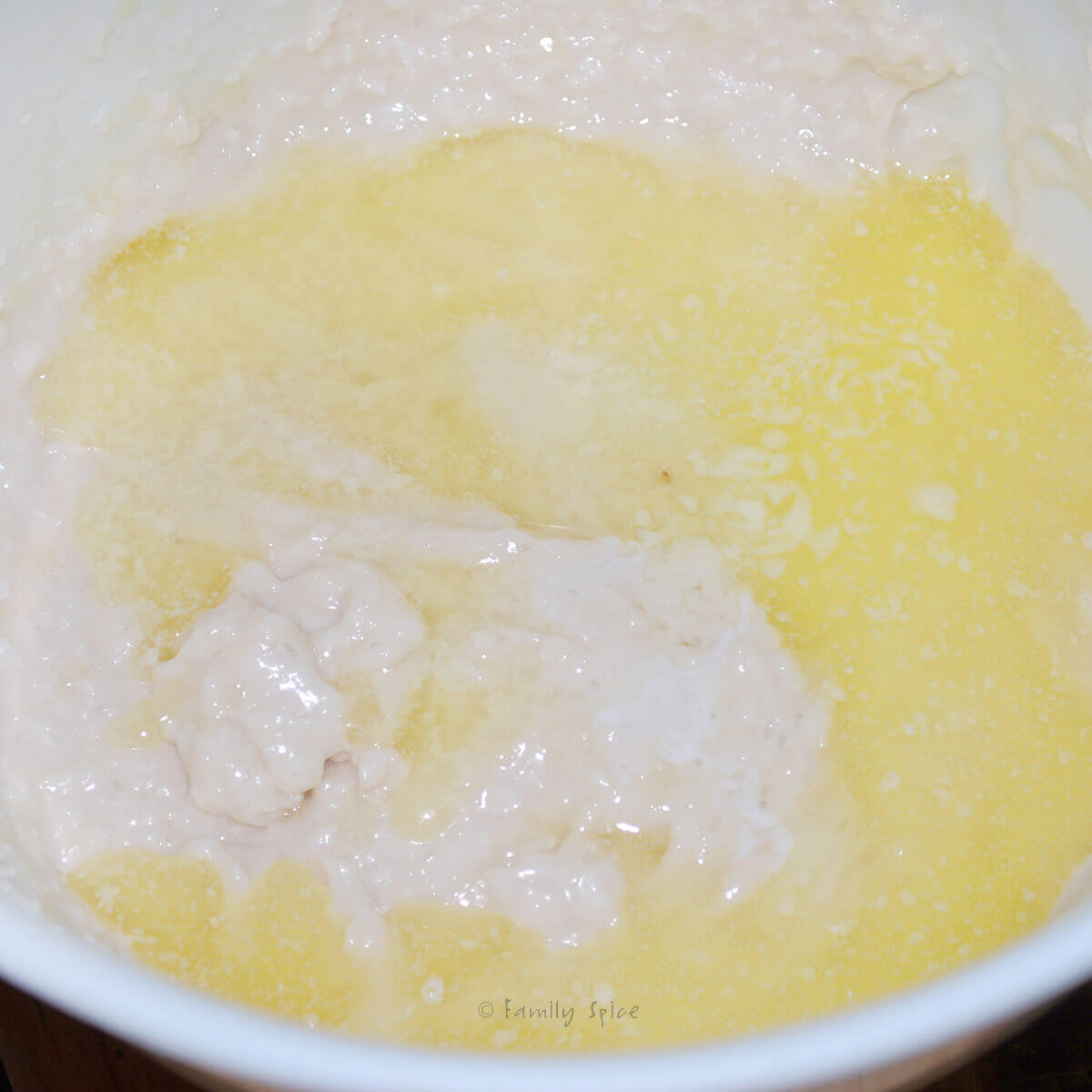 A white mixing bowl with melted butter added to the remaining ingredients to make coconut thin cookies