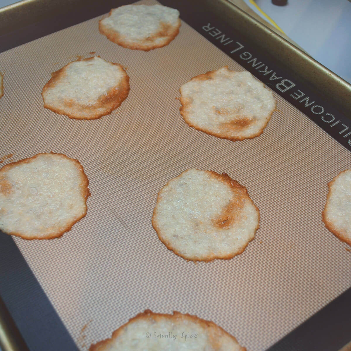 A baking sheet lined with silicone baking mat with freshly baked coconut thin cookies on it