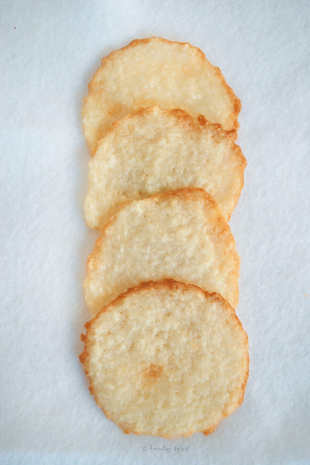 Top view of four coconut thin cookies on a white surface