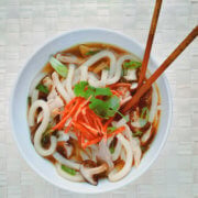 Top view of a bowl of chicken udon soup with chopsticks in it